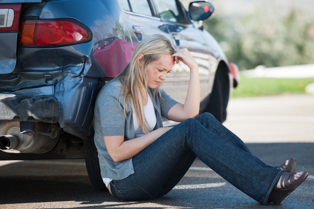 Woman sits next to car after a car accident causing her back pain